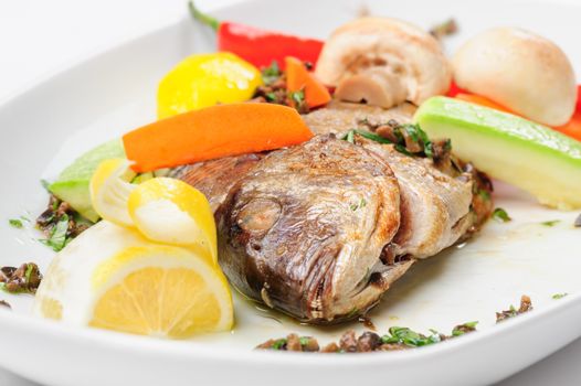 Roasted dorada fish with vegetables and mushrooms on white plate