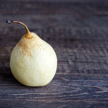 One yellow pear lying on a wooden surface. Selective focus, low key.