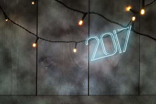 Neon text spelling 2017 on a wooden background with festive lights