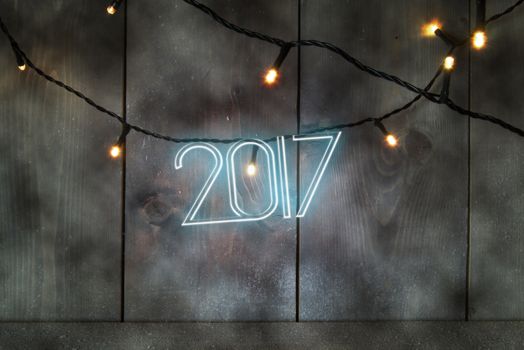 Neon text spelling 2017 on a wooden background with festive lights