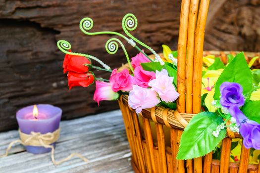 beautiful flowers plastic in a basket on brown wooden background