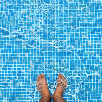 Bare feet cooling off in the pool relaxing concept - square composition