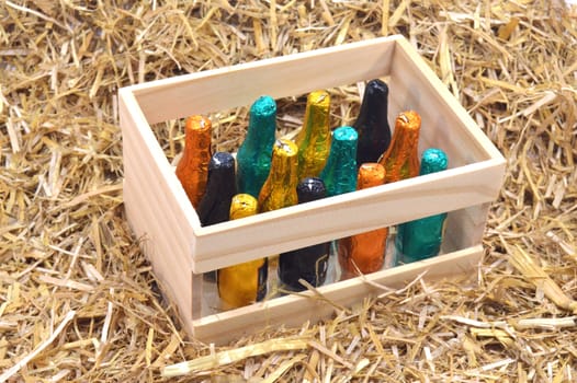 Wooden box of twelve bottles of chocolate filled with liqueur on a background of straw