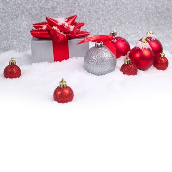 Red and silver christmas balls and gift in snow on glitter background