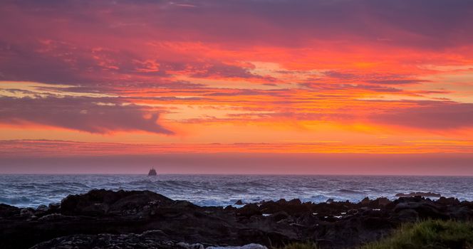 Beautiful sunset off the coast in South Africa with fishing boat on horizon