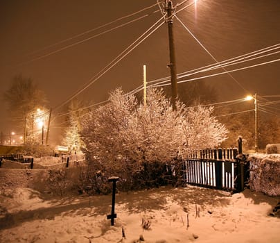 Winter cottages in country landscape at night with glowing lamp light