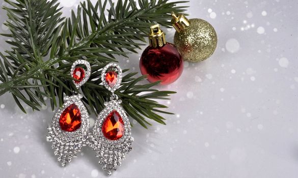 earrings with red stones  on a branch of a Christmas tree with a ball on an abstract background