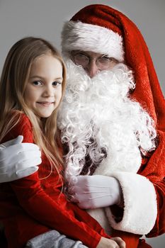 Smiling child girl sitting on the lap of Santa Claus