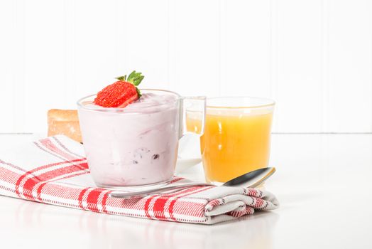 Cup of strawberry greek yogurt served with orange juice.