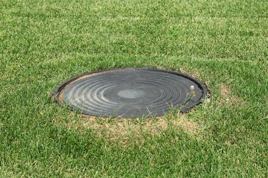 Metal manhole in a background of green grass on the field.