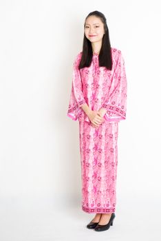 Portrait of young southeast Asian woman in traditional Malay batik dress smiling, standing on plain background.