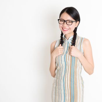 Portrait of young Asian woman in traditional qipao dress smiling, celebrating Chinese Lunar New Year or spring festival, standing on plain background.