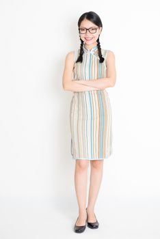 Portrait of young Asian girl in traditional qipao dress smiling, full length standing on plain background.