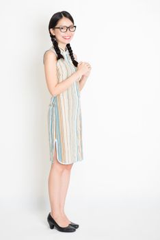 Portrait of young Asian girl in traditional qipao dress greeting, celebrating Chinese Lunar New Year or spring festival, full length standing on plain background.