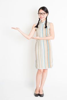 Portrait of young Asian girl in traditional qipao dress hands holding something, full length standing on plain background.