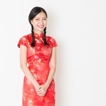 Portrait of young Asian woman in traditional qipao dress smiling, celebrating Chinese Lunar New Year or spring festival, standing on plain background.