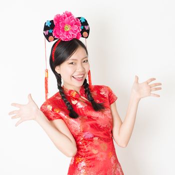 Young Asian woman in traditional qipao dress holding mandarin orange and smiling, celebrating Chinese Lunar New Year or spring festival, standing on plain background.