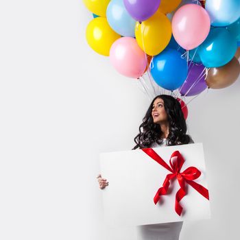 Young smiling woman with balloons and big gift box