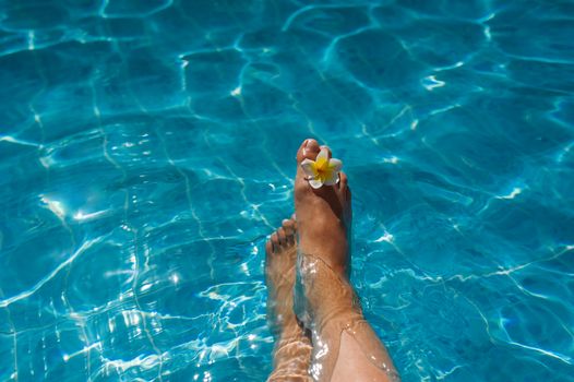 womans legs with flower in blue pool.