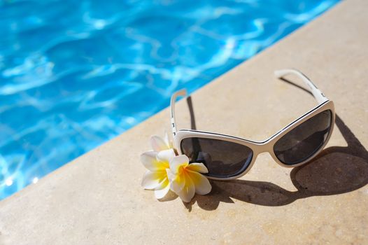 sunglasses and white flowers of bougainvillea near pool.