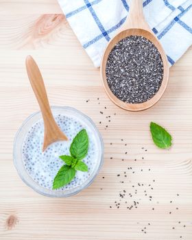 Nutritious chia seeds in glass bowl with wooden spoon for diet food ingredients setup on wooden background .