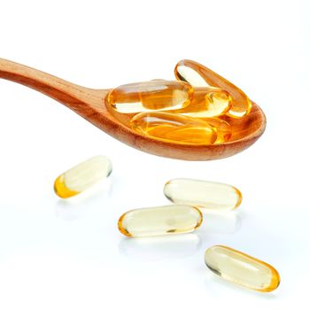 Spoonful of gel capsules of omega 3. Close up capsules fish oil in wooden spoon .The supplement high vitamin E, omega 3 and DHA . Capsules fish oil with selective focus isolate on white background.