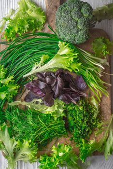 Broccoli, lettuce, basil, onion, dill on cutting board vertical