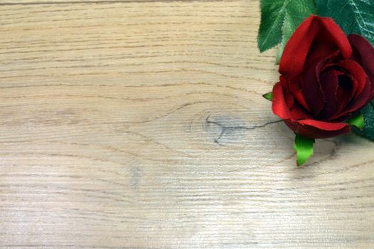 Red rose with wedge leaves on a brown wood background