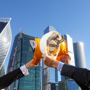 Group of business people clinking their helmets as a success on skyscrapers background, construction finished concept