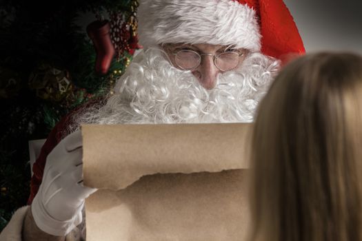Santa Claus holding list on old paper and girl choosing gift