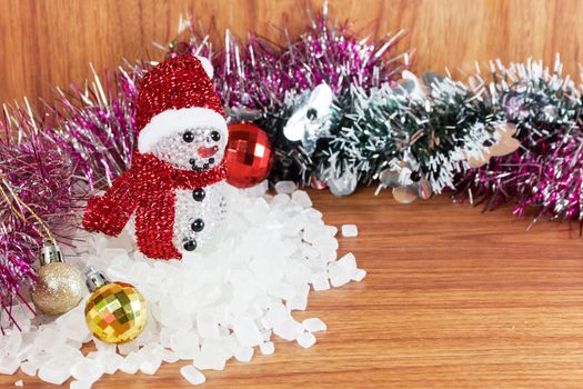 Snow Man on a pile of white crystalline with white background. Red and yellow Christmas Balls Ornaments on wood,