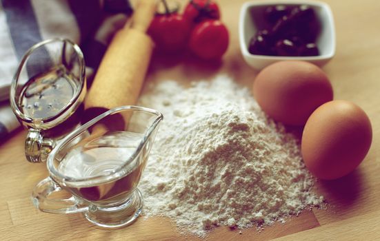 Preparing Homemade Fresh Pasta Dough with Black Olives, Tomatoes and Olive Oil with Herbs closeup on Wooden Table. Focus on Top of Flour