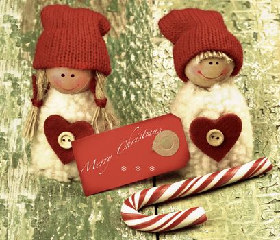 Christmas Decoration Concept with Handmade Dolls in Knit Hats, Striped Sweet Cane and Greeting Card with Inscription closeup on Rustic Cracked background. Retro Toned