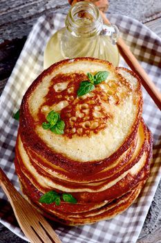 Stack of Delicious Homemade  Pancakes with Mint Leafs, Honey in Glass Container, Wooden Fork and Honey Dipper in Checkered Tray closeup. Top View  on Wooden background