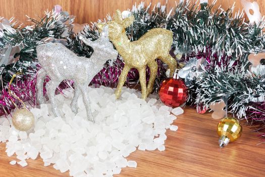 Deer color silver and gold on a pile of white crystalline. Red and yellow Christmas Balls Ornaments on wood,