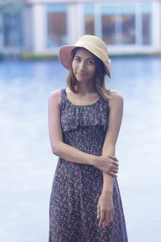 portrait of young beautiful asian tan skin woman smiling face wearing straw hat standing beside water pool in raining day 