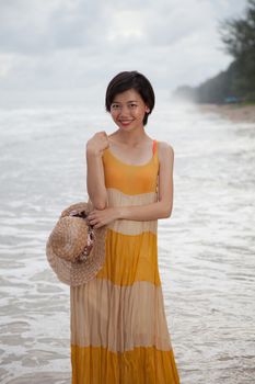 portrait of young asian woman wearing long dress with smiling face standing on sea beach relaxing emotion 