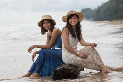 portrait of young beautiful asian tan skin  woman wearing fashion straw hat sitting on wood lock at sea beach with relaxing emotion