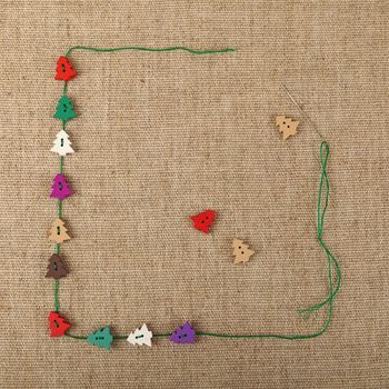 Festive template of handicraft colorful wooden Christmas tree button decorations and thread over linen canvas, close up, elevated top view, copy space