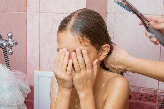 Girl covering her face with her hands while Mom washes her long hair