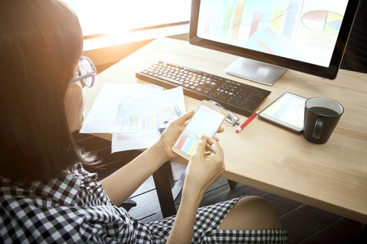 woman and smart phone in hand looking to computer on table for people home working concept