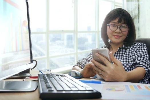 asian working woman looking to smart phone and smiling happiness emotion for office life theme