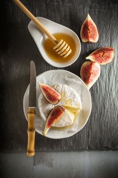 A wheel of melted brie covered in sliced figs and honey  on a stone plate.