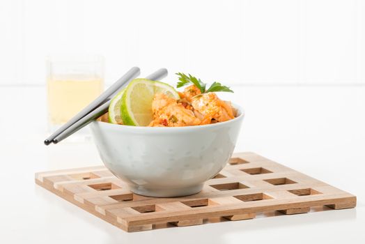 Bowl of spicy pad thai with lime wedges.