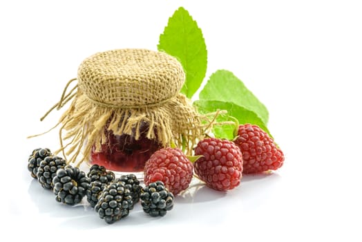 Blackberries and raspberries and green leaves around the jar isolated on white background