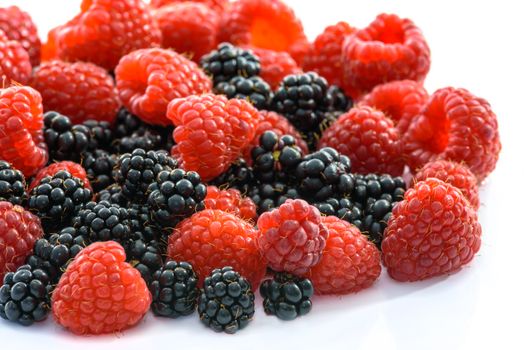 Raspberries and blackberries scattered on a white background