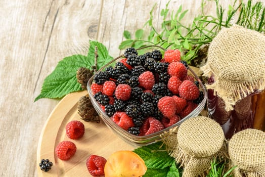 Bowl full of blackberries and raspberries, and preparations homework on a wooden table vintage