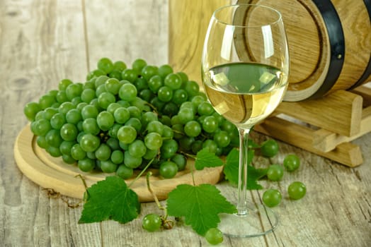 Semi sweet white wine in the cup  next to fresh grapes and a wooden barrel