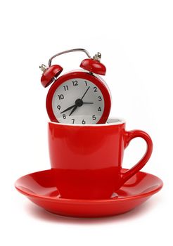 Coffee time concept, small red metal alarm clock with red bells in coffee cup or teacup with saucer, over white background, close up, low angle side view