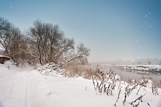 Winter misty river. Snow and frost. Snowy road. Overcast snowy weather. Cloudy cold January day.
